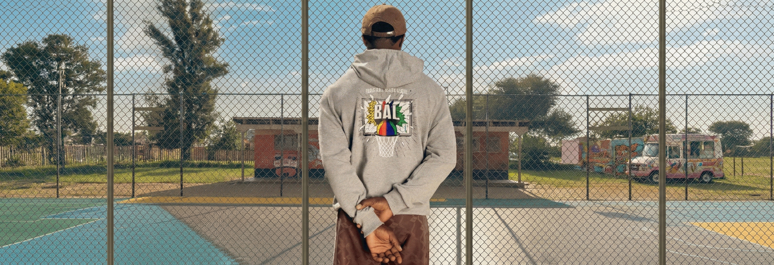 Person standing on a tennis court with a colorful hoodie and cap, looking out over the court.